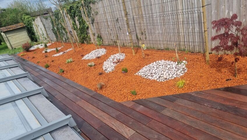 Aménagement paysager avec paillis orange et pierres blanches le long d'une terrasse en bois à Montauroux, Var